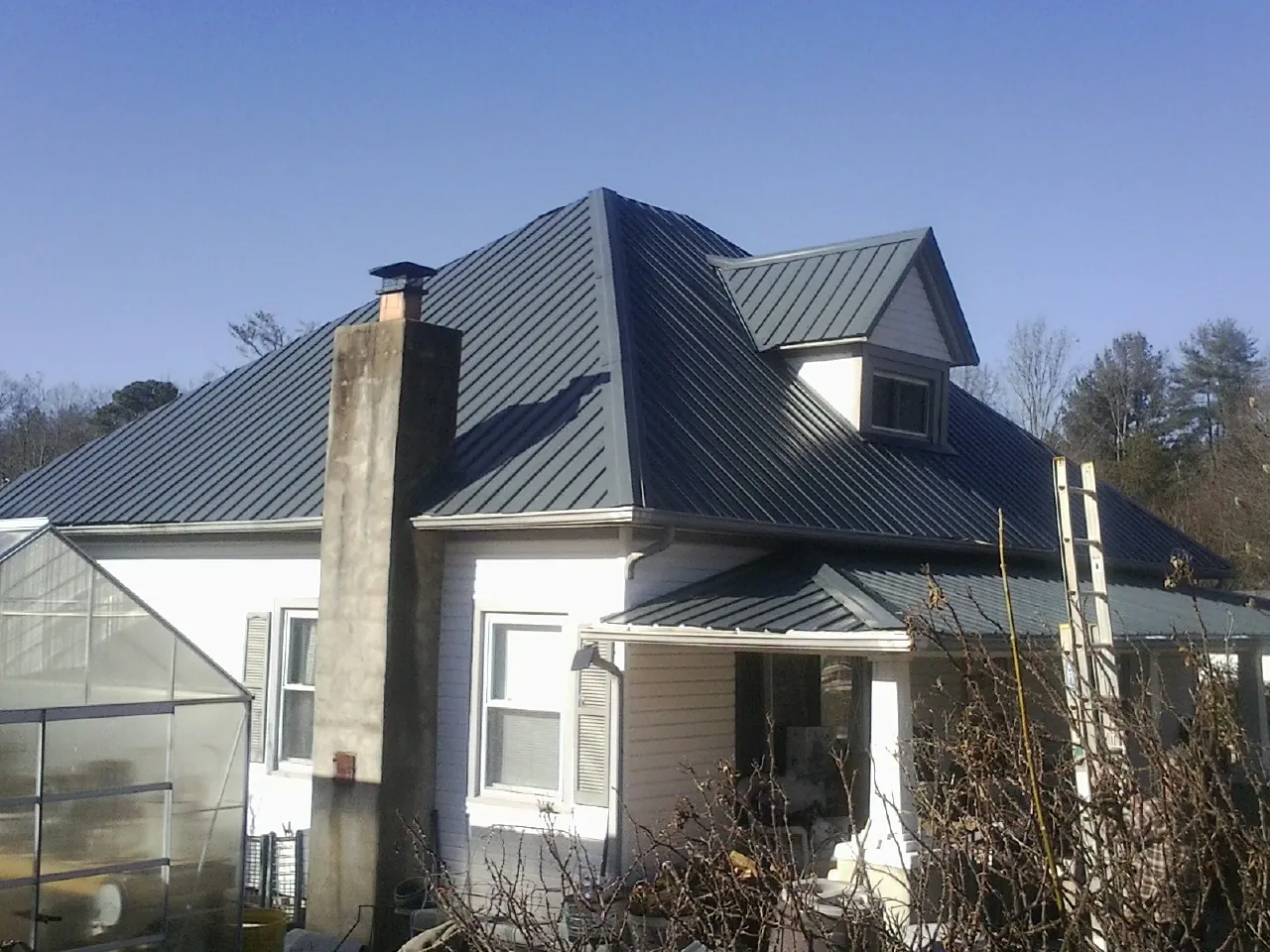 Dark blue standing seam metal roof on a white farmhouse with dormer — Slate & Tile Roof Repair by Roofing Brothers in Cowansville