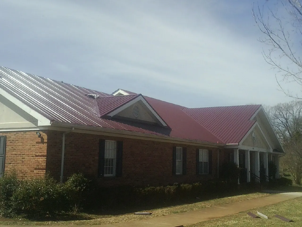 Red metal roof with gabled entries on a long brick building, from a Hail Damage Roof Repair job in Cowansville