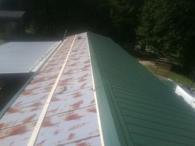 Old rusted panels beside newly installed green metal roofing — Wind Damage Roof Repair by Roofing Brothers in Cowansville