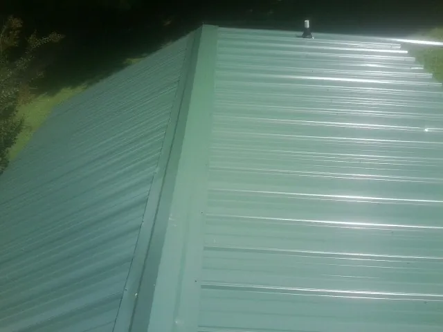 New green metal panels meeting at the ridge of a roof — Flat Roof Repair work by our crew in Cowansville