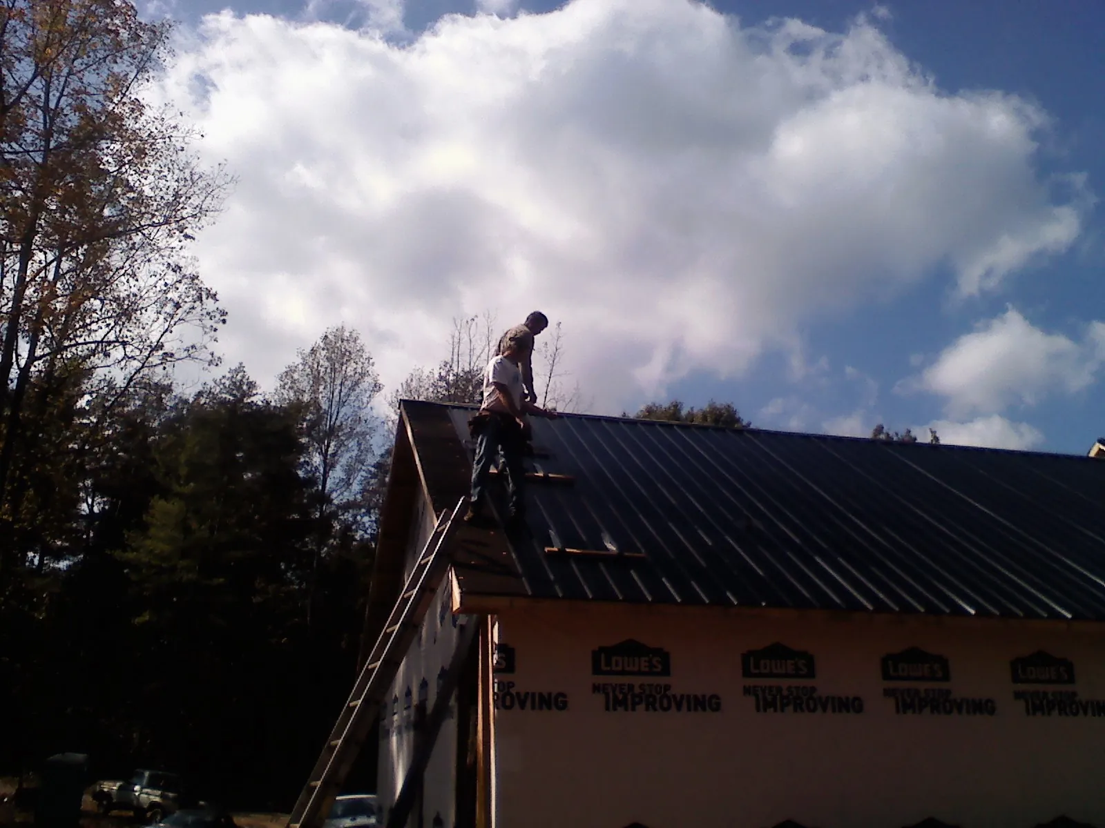 Roofer fastening dark metal panels high against a cloudy sky, from a Roof Inspection job in Cowansville