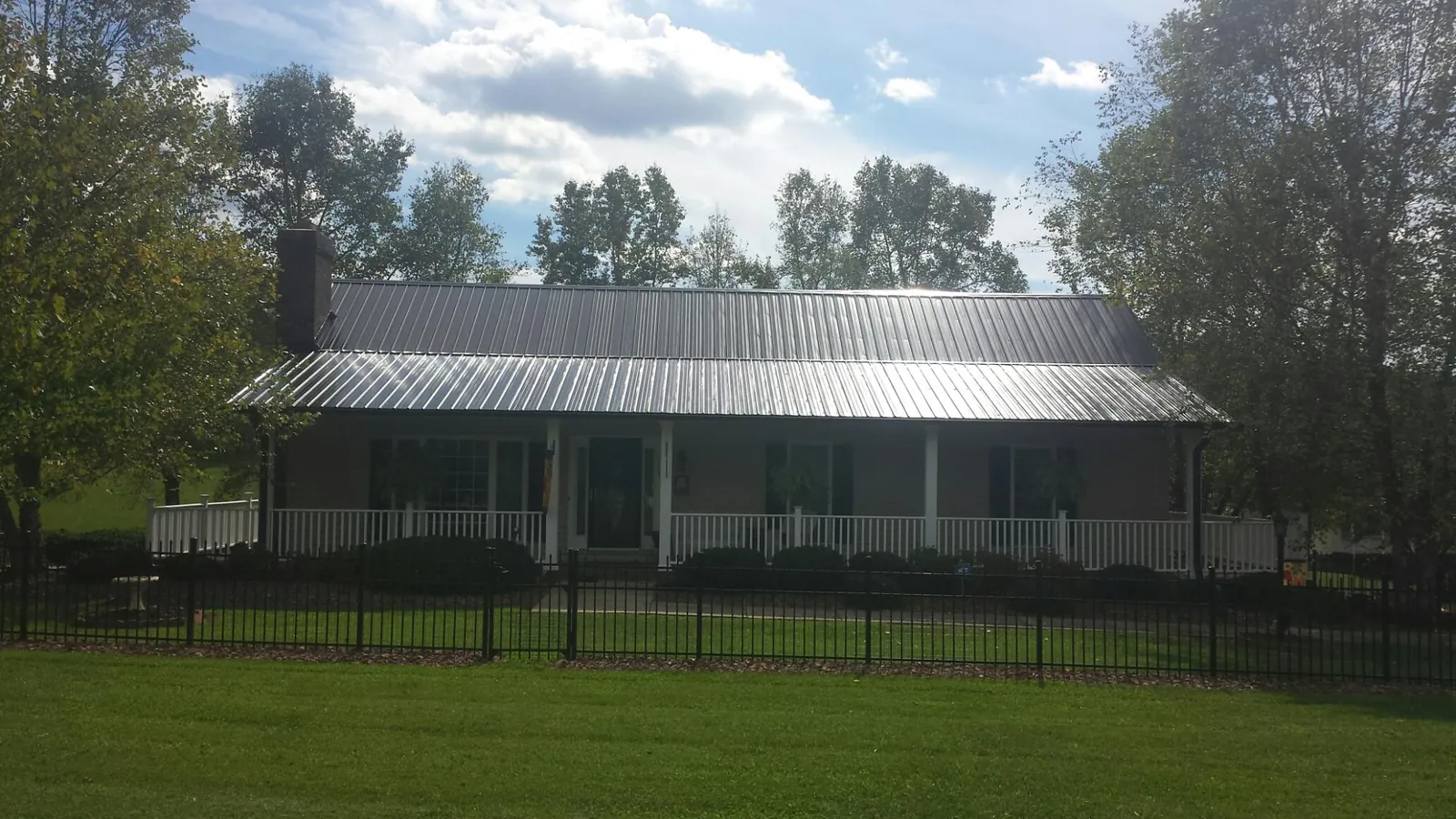 Gray metal roof on a brick ranch with a full width front porch — Gutter Guard Installation work by our crew in Cowansville