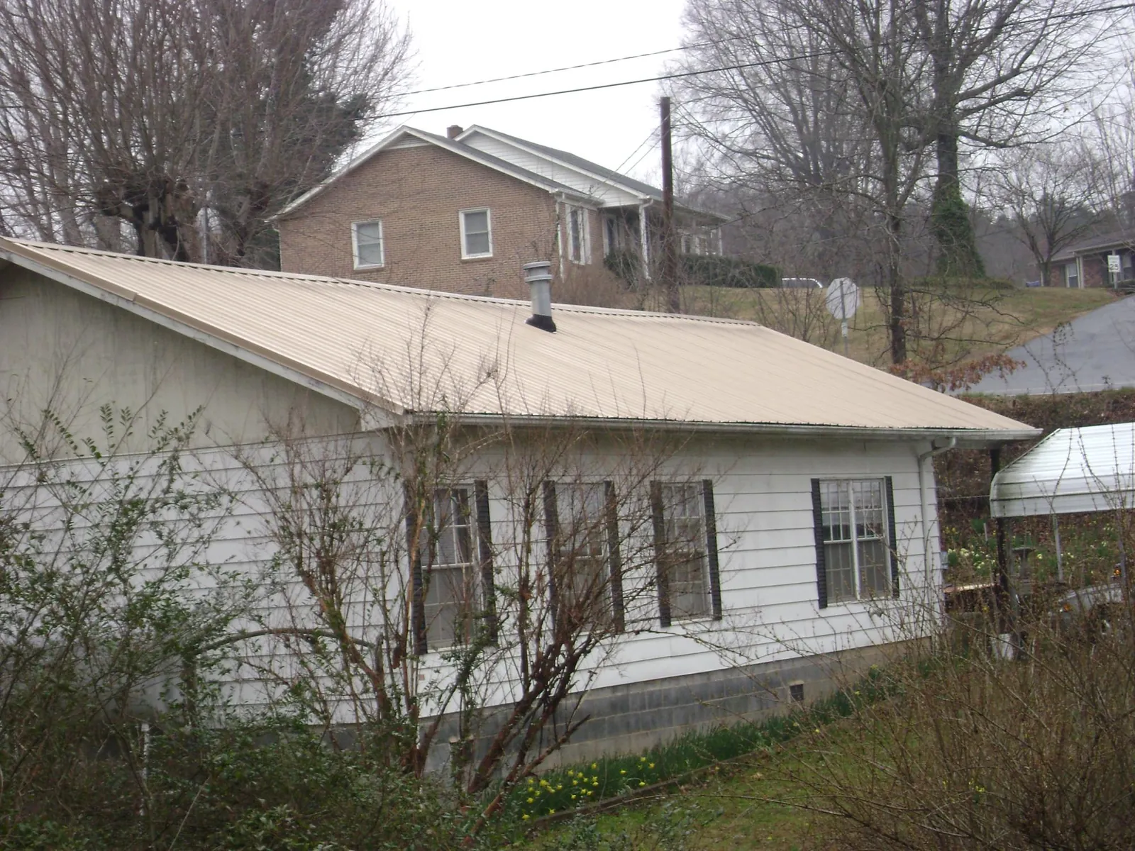 Tan metal roof on a white sided house set into a hillside — Commercial Roofing by Roofing Brothers in Cowansville