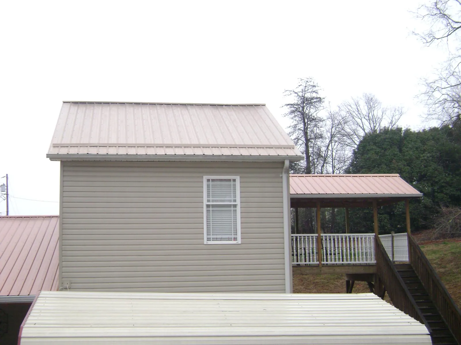 Tan metal roofs on a two story addition and attached porch, from a Roof Replacement job in Cowansville
